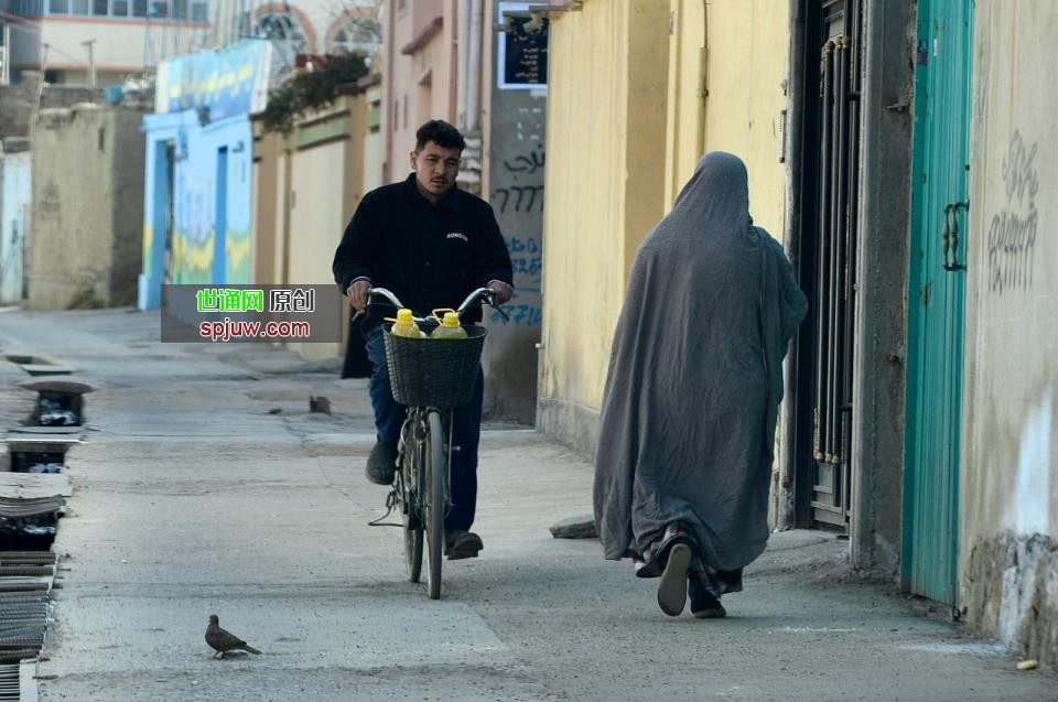 A man rides a bicycle past a woman walking along a street in Kabul, March 19, 2022. (AFP Photo)