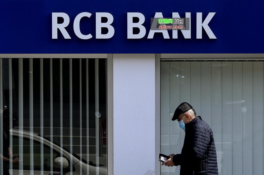 A man uses his cell phone as he walks outside of a branch of RCB, Russian Commercial Bank, in the divided capital of Lefkoşa (Nicosia), the island of Cyprus, March 24, 2022. (AP Photo)